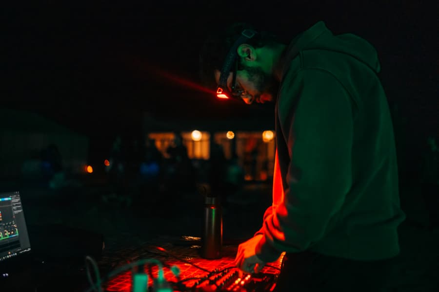 Disektor performing the live set at the mixer, lit red by the desk lamp