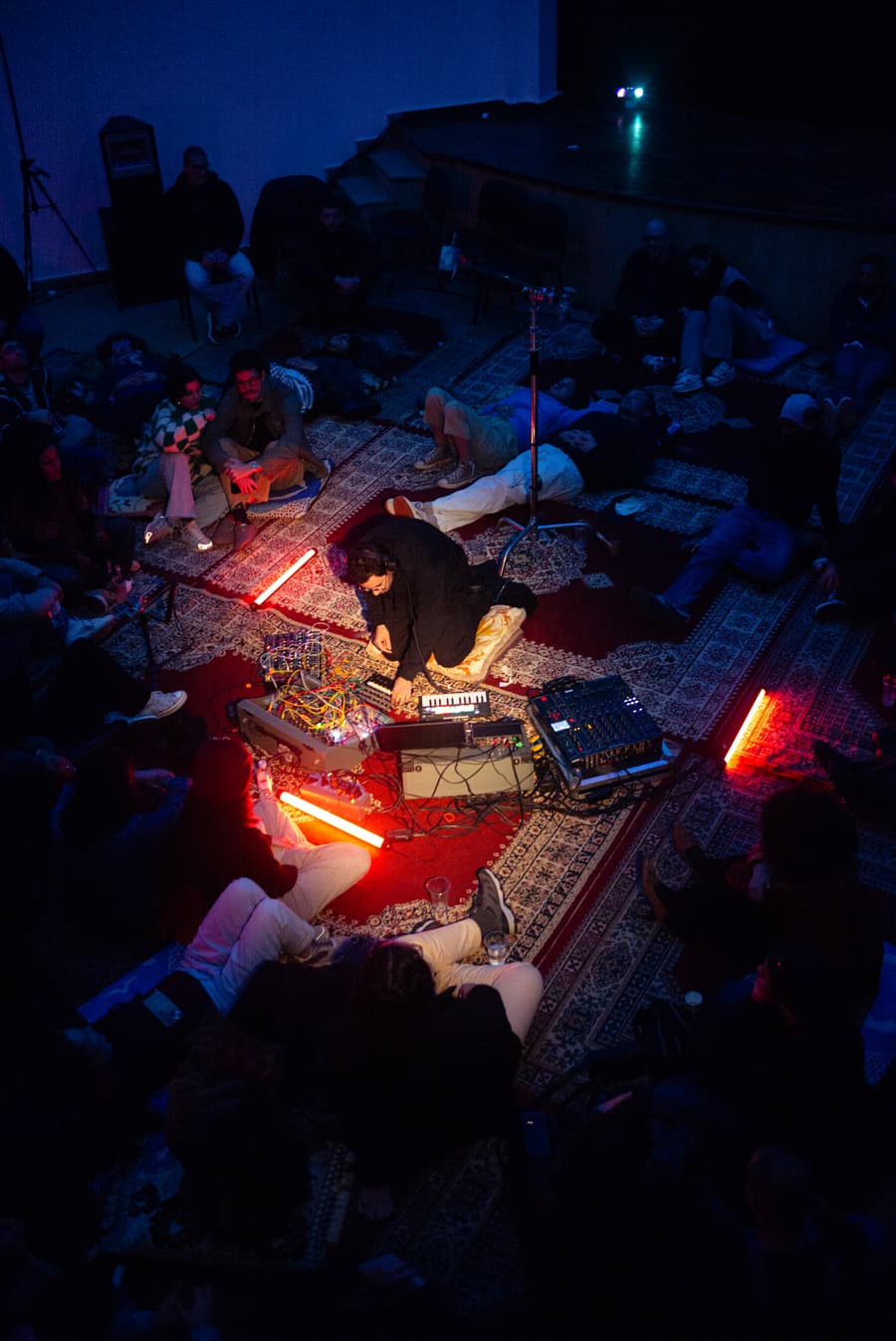 Disektor playing a modular set from the floor at La Coupole, the audience lying on rugs around the rig under red neon